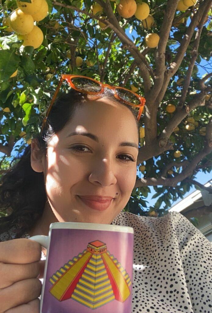 Berenice Santos smiling under a fruit tree holding a mug